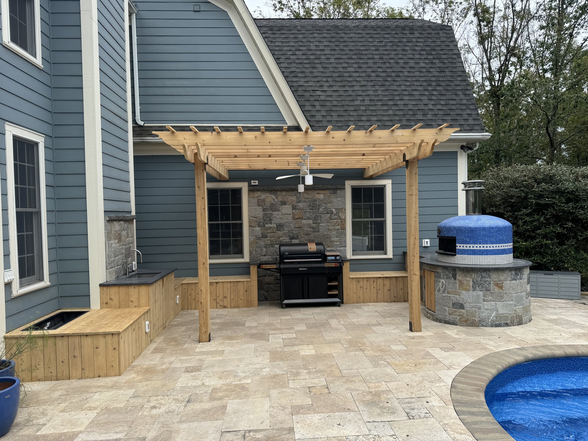 Cedar pergola, stone outdoor kitchen and travertine paver patio installed by Dutchess Lawns & Masonry